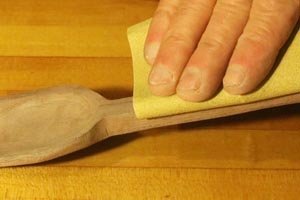Using sandpaper to hand sanding a wooden spoon.